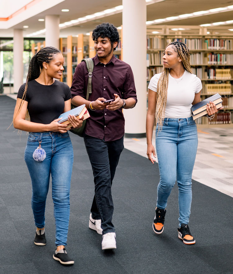 3 students walking though the library